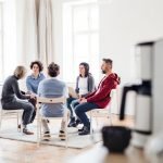 Serious men and women sitting in a circle during group therapy, talking.