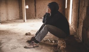 man in dispair sitting on the ground in an abandoned warehouse