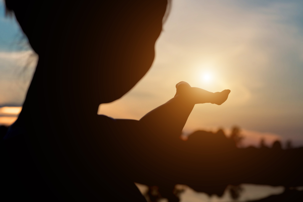 Silhouette of person holding out hand to capture the setting sun