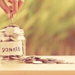 Hand putting Coins in glass jar for giving and donation concept